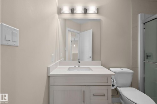 Bathroom vanity with a white countertop and integrated sink, chrome faucet, and a large mirror with a three-light vanity fixture - 309 625 Leger Way, Edmonton, AB 