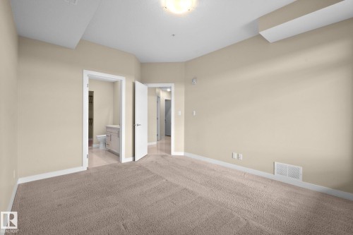 Neutral-toned carpet flooring and light beige walls create an expansive interior space - 309 625 Leger Way, Edmonton, AB 