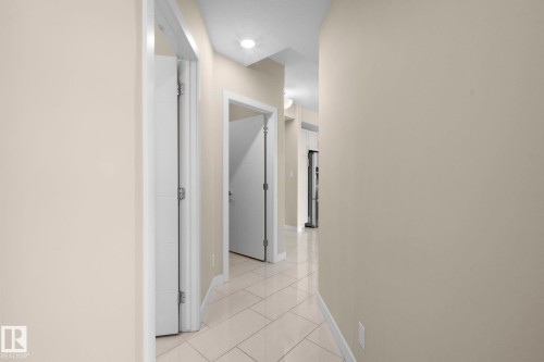 Hallway featuring neutral wall tones, recessed lighting, white trim, and light-toned tile flooring - 309 625 Leger Way, Edmonton, AB 