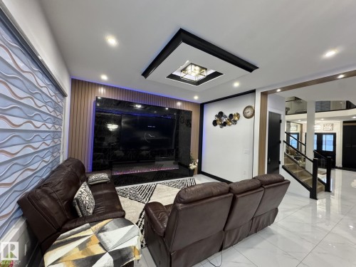 Living area featuring a ceiling inset with recessed lighting, a built-in media wall with dark stone-finish paneling, and wood-finish accent wall panels - 2123 18 Avenue, Edmonton, AB 