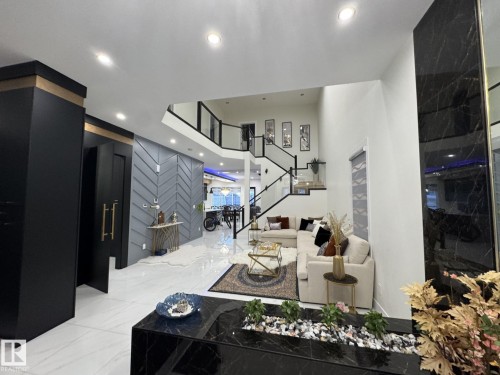 Two-story foyer featuring an open staircase with glass panels and dark railings, recessed lighting, and a chevron-patterned accent wall - 2123 18 Avenue, Edmonton, AB 