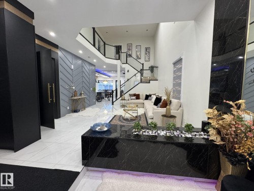 Two-story foyer featuring marble-look flooring, a black marble-look planter, a chevron-pattern accent wall, and a multi-level staircase with glass railings - 2123 18 Avenue, Edmonton, AB 