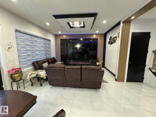 Living area featuring a dark marble-finish media wall with built-in fireplace, a rectangular coffered ceiling with recessed lighting, and light wood-tone slat wall accents - 2123 18 Avenue, Edmonton, AB 