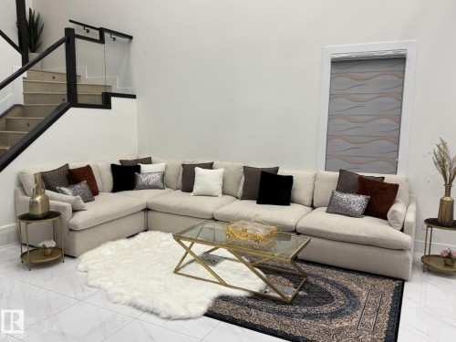 Spacious living area featuring polished tile flooring, a contemporary staircase with glass panel railing and dark wood-finish newel posts, and a window with a patterned roller shade - 2123 18 Avenue, Edmonton, AB 