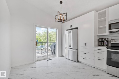 Kitchen featuring white flat-panel cabinetry, stainless steel appliances, and a white tile backsplash - 1 Hunt Court, St. Albert, AB 