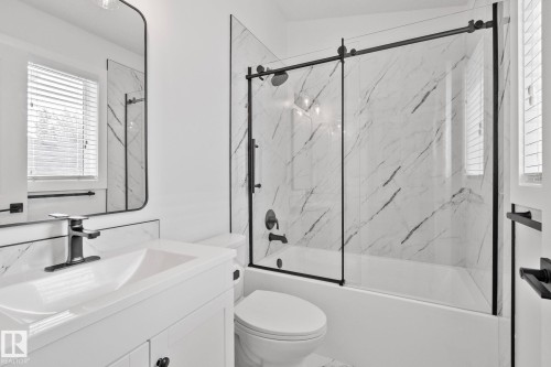 Full bathroom featuring a white vanity with integrated sink, black-framed mirror, and a tub-shower combination with sliding glass doors - 1 Hunt Court, St. Albert, AB 