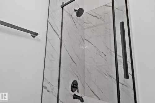 Shower enclosure featuring white marble-look tile, matte black fixtures, and a clear glass panel with a black frame - 1 Hunt Court, St. Albert, AB 