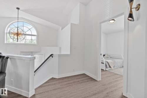 Upper-level landing featuring vaulted ceilings, an arched window, a contemporary chandelier, wood-finish flooring, and a modern wall sconce - 1 Hunt Court, St. Albert, AB 