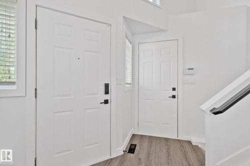Entryway featuring two paneled doors, matte black hardware, wood-finish flooring, and a white staircase with a black handrail - 1 Hunt Court, St. Albert, AB 