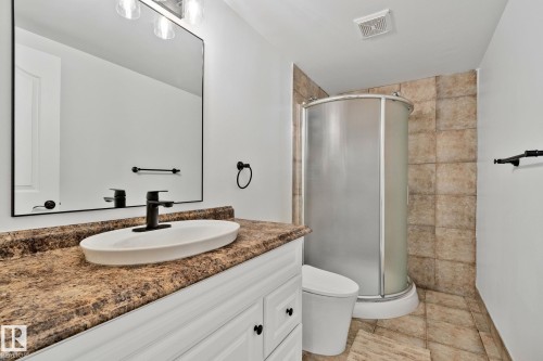 Bathroom featuring a curved glass shower enclosure with tiled walls, a vanity with a textured countertop, a matte black faucet, an oval vessel sink, and a large rectangular mirror - 1 Hunt Court, St. Albert, AB 