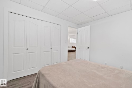 White bi-fold closet doors with black hardware, wood-finish flooring, white walls, and a drop ceiling - 1 Hunt Court, St. Albert, AB 