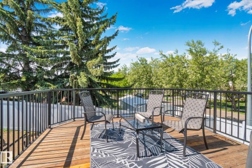 Spacious outdoor deck featuring wood-finish flooring, black metal railings, and mature trees - 1 Hunt Court, St. Albert, AB 