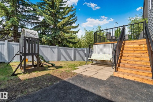 Expansive backyard featuring a multi-level deck with wood stairs and black metal railings, a stone patio, and a white privacy fence - 1 Hunt Court, St. Albert, AB 