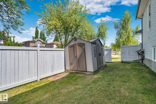 Private grassy side yard featuring a storage shed, a white privacy fence, and a hose reel attached to the exterior siding - 1 Hunt Court, St. Albert, AB 