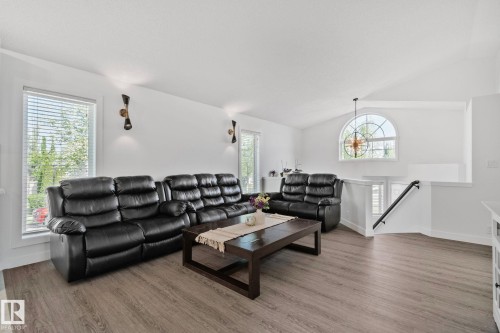 Vaulted ceiling living area featuring wood-finish flooring, a prominent arched window, and a white painted railing - 1 Hunt Court, St. Albert, AB 
