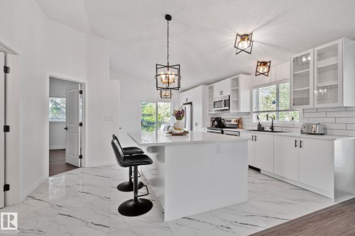 Contemporary kitchen featuring a large central island with seating, white shaker cabinetry, stainless steel appliances, and a subway tile backsplash - 1 Hunt Court, St. Albert, AB 