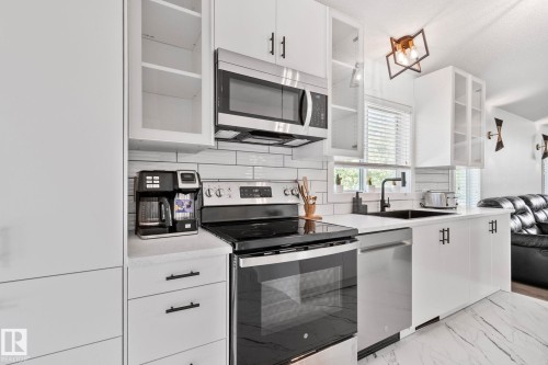 Modern kitchen featuring white cabinetry, stainless steel appliances, white subway tile backsplash, and light-toned countertops - 1 Hunt Court, St. Albert, AB 