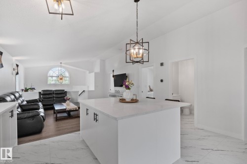 White kitchen island with a light-toned countertop, matte black hardware, and an overhead geometric pendant light - 1 Hunt Court, St. Albert, AB 