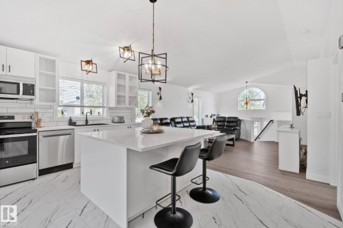 Contemporary kitchen featuring a large center island, white cabinetry, integrated stainless steel appliances, a subway tile backsplash, and elegant geometric lighting fixtures - 1 Hunt Court, St. Albert, AB 