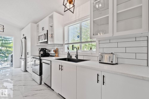 Modern kitchen featuring white cabinetry, stainless steel appliances, a black sink and faucet, white subway tile backsplash, and light-toned countertops - 1 Hunt Court, St. Albert, AB 