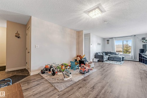 Open-concept living area featuring wood-finish flooring, a large picture window, and a modern ceiling light fixture - 320 534 Watt Boulevard, Edmonton, AB - Indoor Photo Showing Living Room