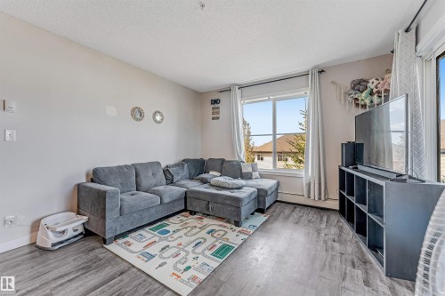 Living area featuring wood-finish flooring, light neutral wall tones, a large window, and a sliding glass door - 320 534 Watt Boulevard, Edmonton, AB - Indoor Photo Showing Living Room