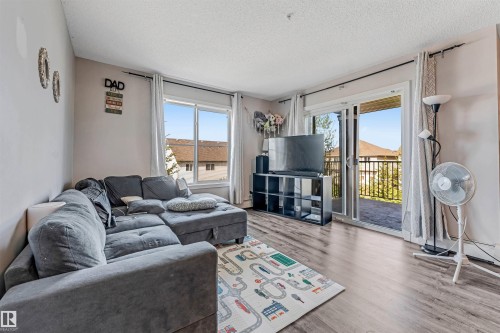 Living area featuring wood-finish flooring, two large windows, and a sliding glass door providing exterior access - 320 534 Watt Boulevard, Edmonton, AB - Indoor Photo Showing Living Room