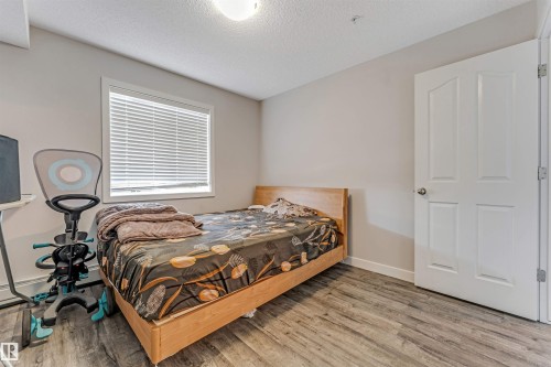 Bedroom featuring wood-finish flooring, a double-panel interior door, and a window with blinds - 320 534 Watt Boulevard, Edmonton, AB - Indoor Photo Showing Bedroom