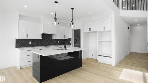 Modern kitchen featuring a black central island with a white countertop, white upper and lower cabinetry, a dark patterned backsplash, and light wood-finish flooring - 803 30 Avenue, Edmonton, AB 