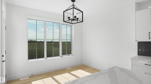 Bright interior with expansive windows, light wood-finish flooring, and a modern black geometric chandelier - 803 30 Avenue, Edmonton, AB 