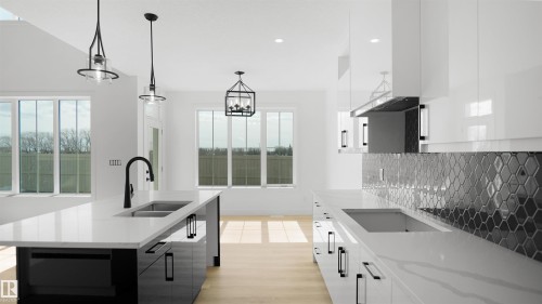 Spacious kitchen featuring an expansive island with dual sinks and a black gooseneck faucet, white countertops, sleek black and white cabinetry, and a black honeycomb tile backsplash - 803 30 Avenue, Edmonton, AB 