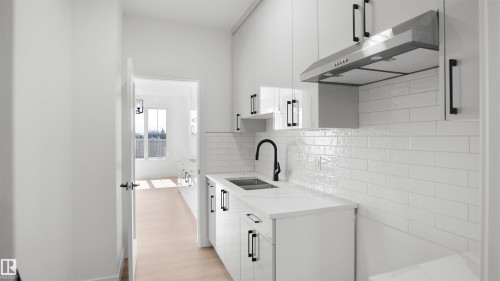 Contemporary kitchen featuring white cabinetry with matte black hardware, a stainless steel range hood, a white subway tile backsplash, a black gooseneck faucet, and light wood-finish flooring - 803 30 Avenue, Edmonton, AB 