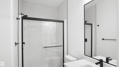 Modern bathroom featuring a black-framed glass shower enclosure with a rainfall showerhead, white subway tile with subtle veining, a white toilet, and a vanity with a white countertop and a black single-handle faucet - 803 30 Avenue, Edmonton, AB 