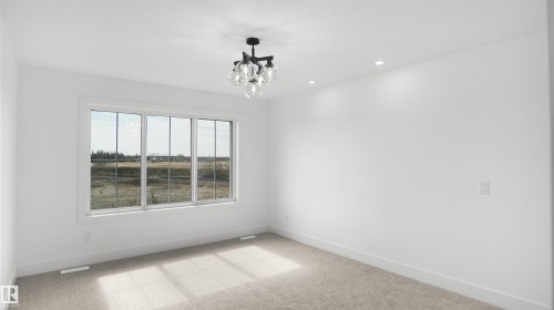 Spacious room featuring a large three-panel window, light neutral carpeting, recessed ceiling lighting, a modern black and glass chandelier, and white baseboards - 803 30 Avenue, Edmonton, AB 