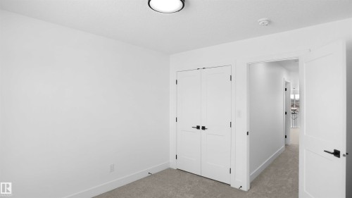 Room featuring light gray carpeting, crisp white walls, a flush-mount ceiling light, and white bi-fold closet doors with matte black hardware - 803 30 Avenue, Edmonton, AB 