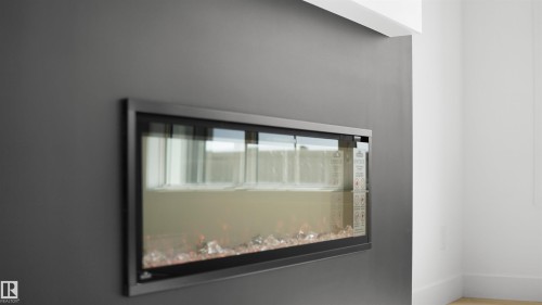 Recessed linear fireplace with a black frame and clear glass panel, featuring decorative fire media - 803 30 Avenue, Edmonton, AB 