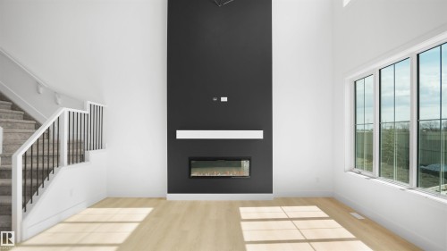 Double-height living area featuring an integrated linear fireplace with a white mantel, light wood-finish flooring, a wall of large windows, and a carpeted staircase with an open railing - 803 30 Avenue, Edmonton, AB 