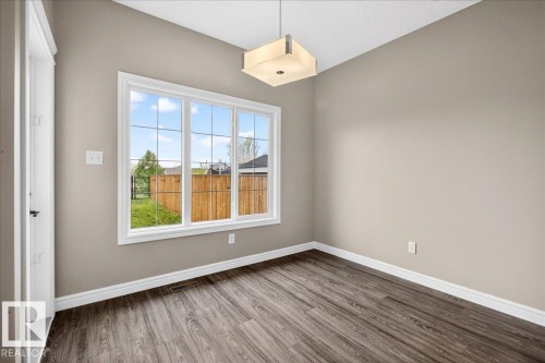 Expansive window with grid panes, wood-finish flooring, neutral wall paint, white baseboards, and a contemporary ceiling fixture - 62 Durrand Bend, Fort Saskatchewan, AB 