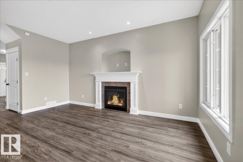 Living area featuring wood-finish flooring, a fireplace with a white mantel and brick surround, and a recessed architectural detail above - 62 Durrand Bend, Fort Saskatchewan, AB 