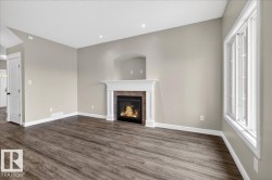 Living area featuring wood-finish flooring, a fireplace with a white mantel and brick surround, and a recessed architectural detail above - 