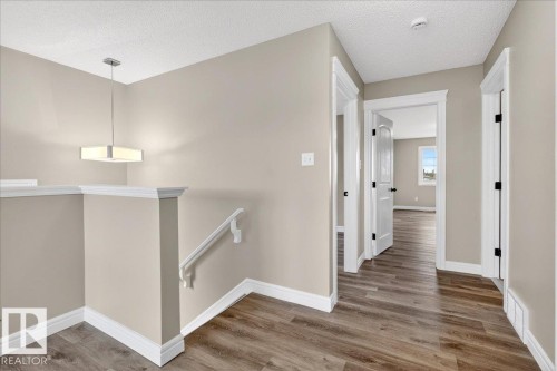 Upper-level hallway featuring wood-finish flooring, light neutral wall paint, white trim, and a contemporary ceiling light fixture - 62 Durrand Bend, Fort Saskatchewan, AB 