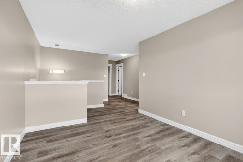 Open interior space featuring wood-finish flooring, neutral wall tones, white trim, and a contemporary pendant light fixture - 62 Durrand Bend, Fort Saskatchewan, AB 