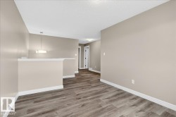 Open interior space featuring wood-finish flooring, neutral wall tones, white trim, and a contemporary pendant light fixture - 