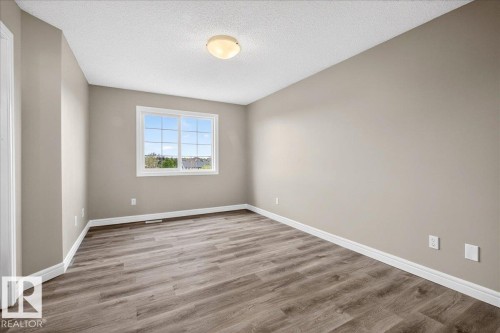 Spacious room featuring neutral painted walls, wood-finish flooring, white baseboards, and a large window with grid pattern - 62 Durrand Bend, Fort Saskatchewan, AB 