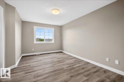 Spacious room featuring neutral painted walls, wood-finish flooring, white baseboards, and a large window with grid pattern - 