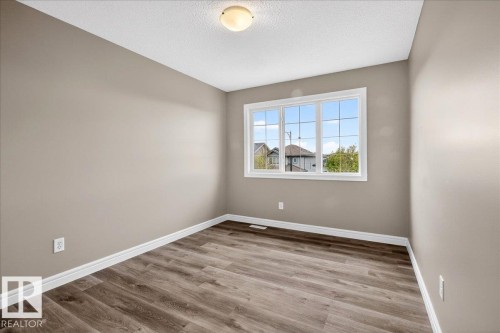 Neutral-toned room featuring a large multi-pane window, wood-finish flooring, crisp white trim, and a ceiling-mounted light fixture - 62 Durrand Bend, Fort Saskatchewan, AB 