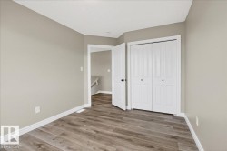 Spacious room featuring wood-finish flooring, light neutral wall paint, white baseboards, and a bi-fold closet with black hardware - 