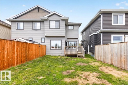 Rear exterior featuring light grey siding, a wood deck with stairs, a sliding glass door, and multiple windows - 62 Durrand Bend, Fort Saskatchewan, AB 