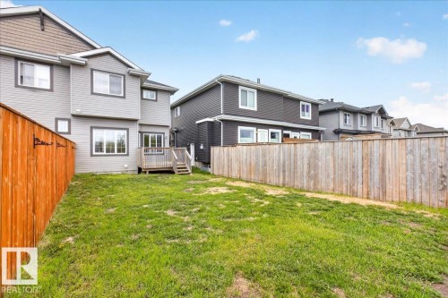 Rear exterior featuring light gray siding with dark trim, a wooden deck with stairs, and a large grassy yard - 62 Durrand Bend, Fort Saskatchewan, AB 