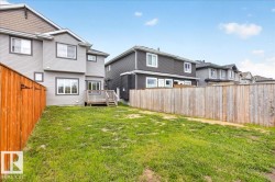 Rear exterior featuring light gray siding with dark trim, a wooden deck with stairs, and a large grassy yard - 